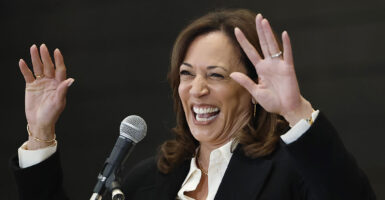 Kamala Harris wearing a black and white suit laughs and puts her hands up