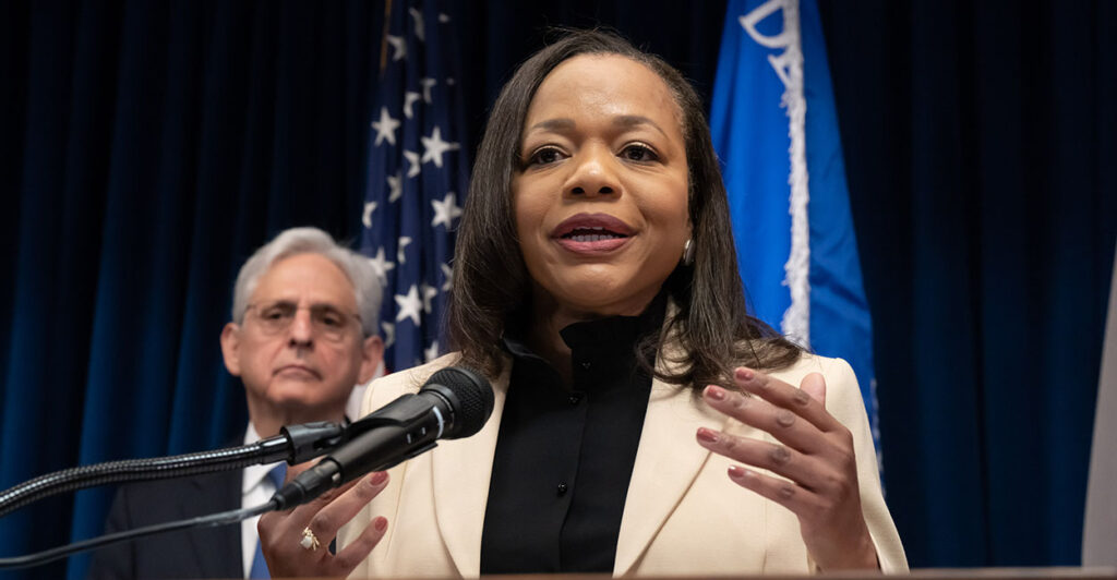 Kristen Clarke in a cream jacket with Merrick Garland behind her.