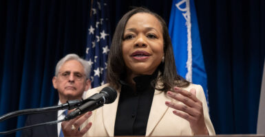Kristen Clarke in a cream jacket with Merrick Garland behind her.