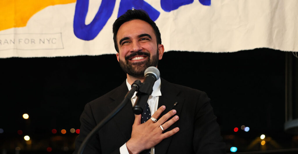Zohran Mamdani puts his hand on his heart while addressing supporters.