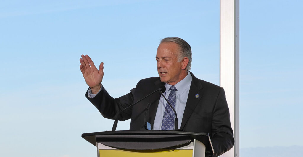 Nevada Gov. Joe Lombardo speaks from a podium, gesturing with his right hand, against a blue sky.