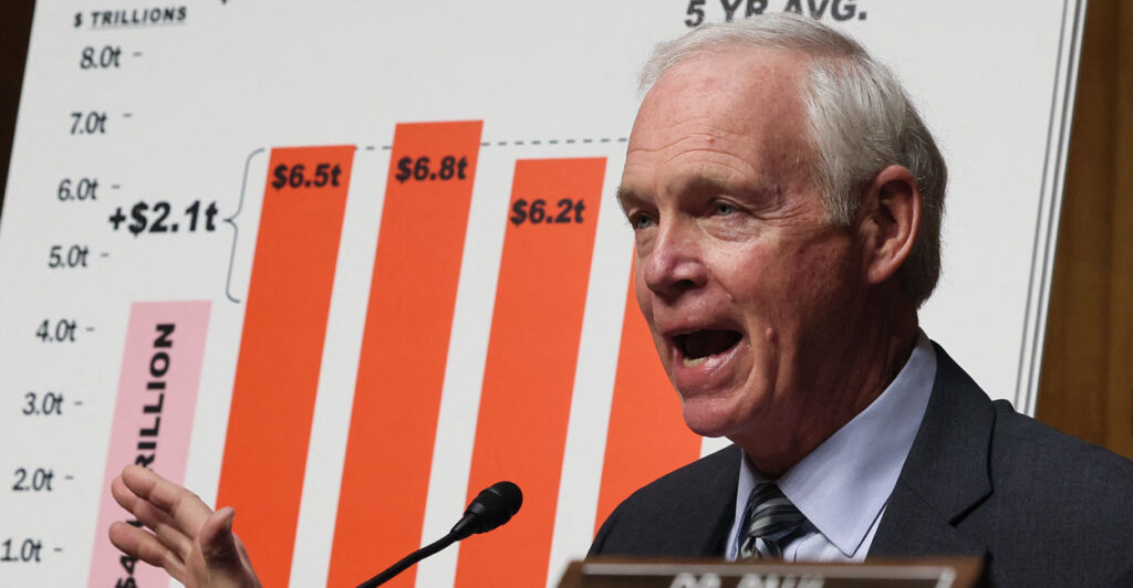 Sen. Ron Johnson speaks in front of a graph featuring orange columns.