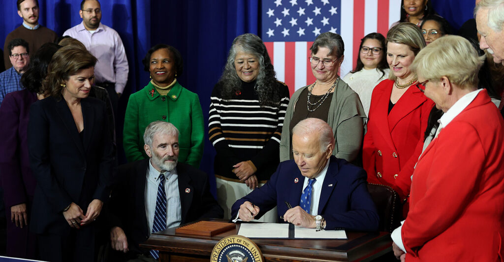 President Joe Biden, surrounded by people, signs an executive order during his final weeks in office.