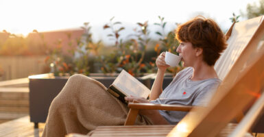 woman sitting on her porch reading a book and sipping coffee