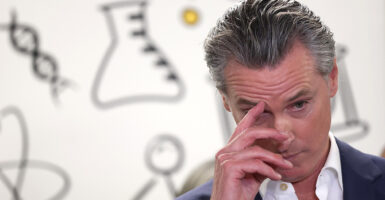 Gavin Newsom, with his hand on his face against a white backdrop with outline drawings of a beaker, DNA strands and other scientific items.