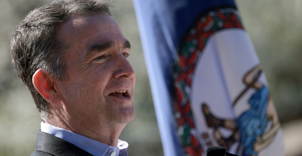 Ralph Northam speaking outdoors with a Virginia flag in the background