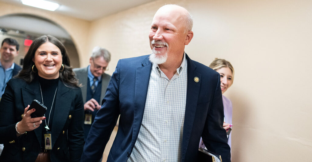 A beaming Rep. Chip Roy talks with reporters while heading down a hallway.