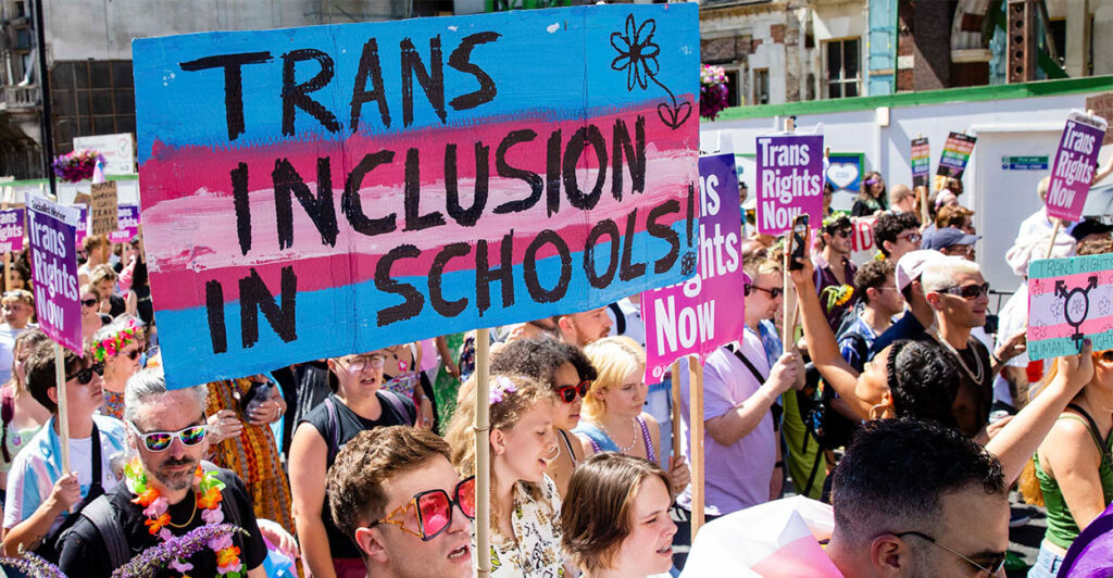 People stand in a crowd with a sign that reads "Trans inclusion in schools."