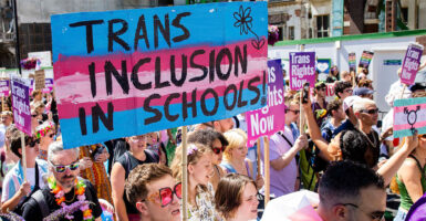 People stand in a crowd with a sign that reads "Trans inclusion in schools."
