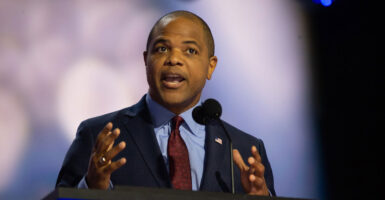 Eric Johnson stands at a podium and gestures with both his hands as he speaks.