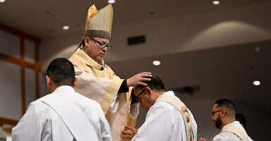 Reverend Alberto Rojas puts his hands on the head of a priest who is kneeling before him during a religious ceremony.