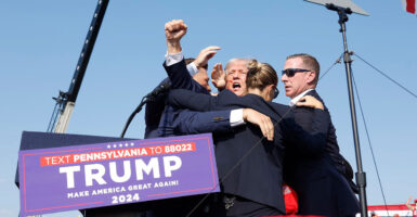 Donald Trump defiantly raises his fist in the air after being shot while Secret Service agents surround him.