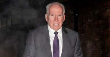John Brennan is wearing a gray suit and tie with his hands at his side as he appears to have a grimace on his face.