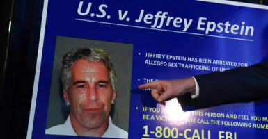 A finger points to a mugshot photo of Jeffrey Epstein on a poster board.