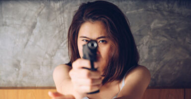 Facing forward, an Asian woman points a pistol in self-defense.