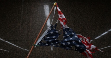 An inverted, torn American flag against black background.