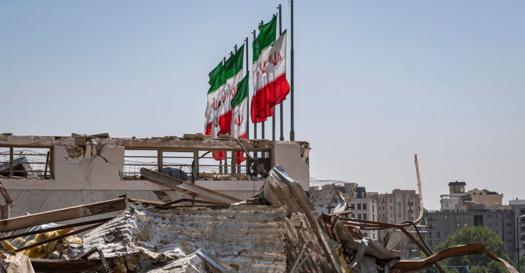 Iranian flags fly over the debris of buildings after an Israeli missile strike.