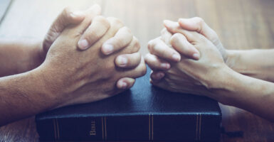 Close-up of male hands and female hands clasped atop a Bible.