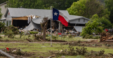 A Texas flies in front of a property wrecked by flooding.