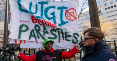 Supporters of Luigi Mangione hold a big banner reading "Luigi Over Parasites."