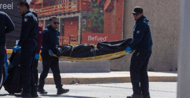 Two Mexican police officers carry the covered body of a murder victim on a stretcher.