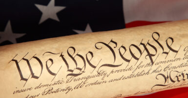 A roll of the U.S. Constitution against a flag backdrop, with "We the People" predominant.