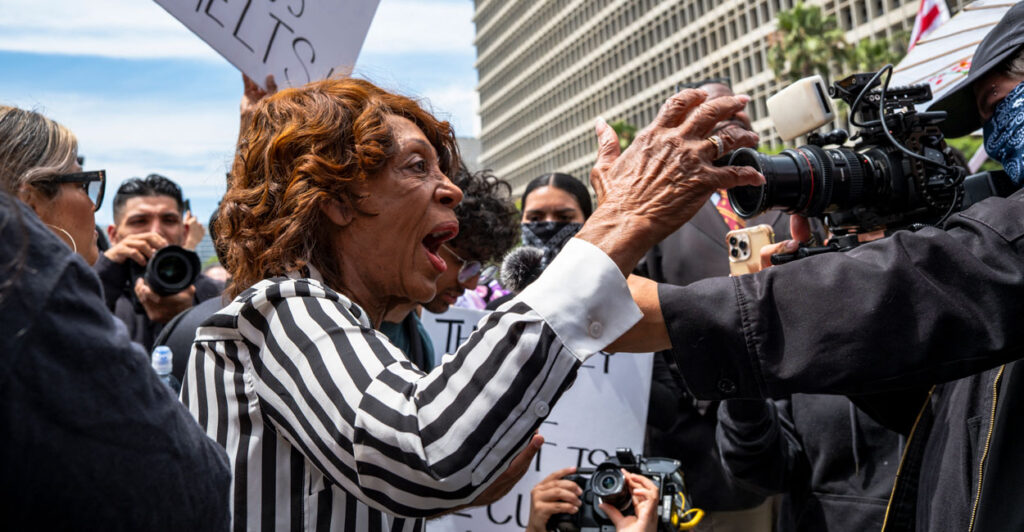Rep. Maxine Waters in a black-and-white striped blouse yelling while talking to reporters.