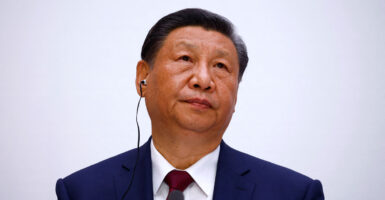 Xi Jinping looking up and to his left against a light gray background.