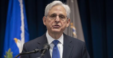 Attorney General Merrick Garland in a dark suit and a blue tie speaks at a podium