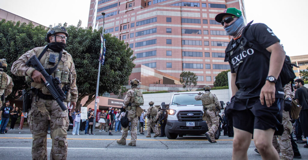 A U.S. Marine and an masked LA protester with a black shirt reading "Mexico" stand face-to-face on an LA street.