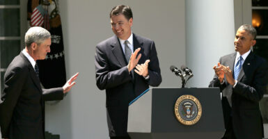 James Comey claps behind podium in White House Rose Garden, flanked by former FBI Director Robert Mueller on his right and President Barack Obama on his left.