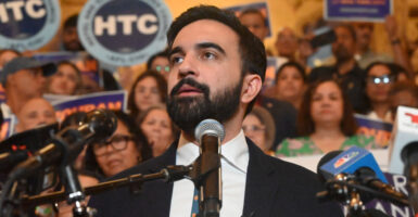 Democratic mayoral candidate Zohran Mamdani lifts his chin as he delivers a speech. Behind him are supporters.