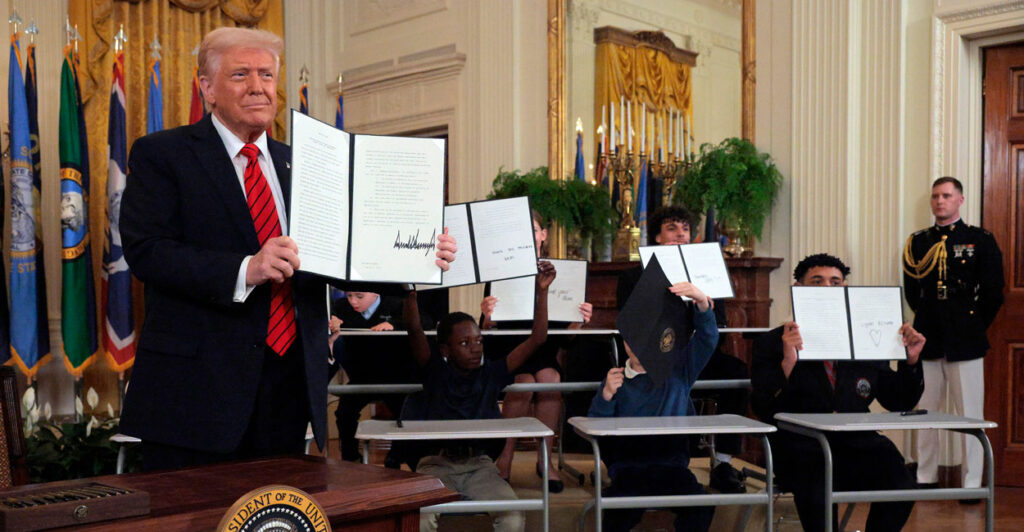 President Trump holds up his executive order reducing the size of the Department of Education. Children behind him also hold up copies of the executive order.