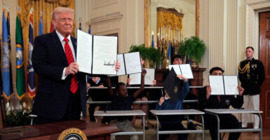 President Trump holds up his executive order reducing the size of the Department of Education. Children behind him also hold up copies of the executive order.