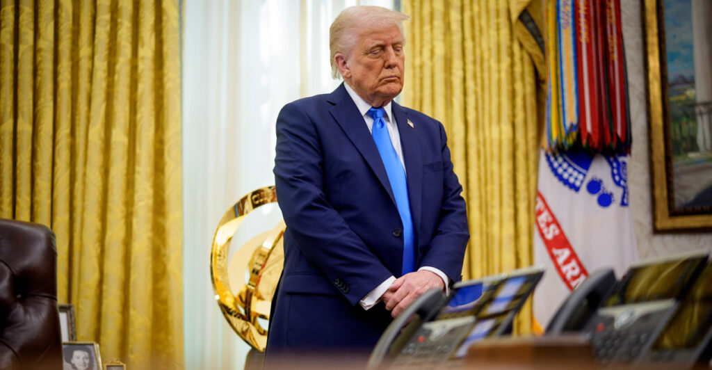 President Donald Trump stands with eyes closed in prayer in Oval Office.