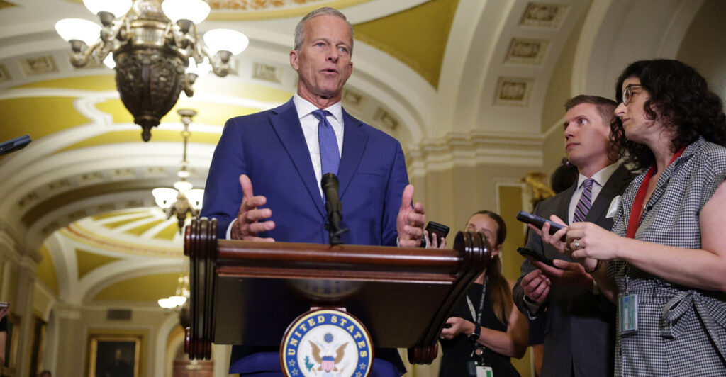 Senate Majority Leader John Thune speaks behind a podium to reporters.