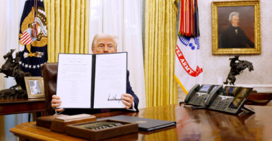 President Donald Trump in Oval Office holds up signed executive order.