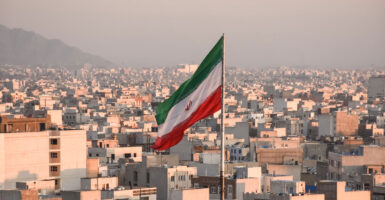 An Iranian flag waves with a cityscape of Tehran, Iran, as backdrop.