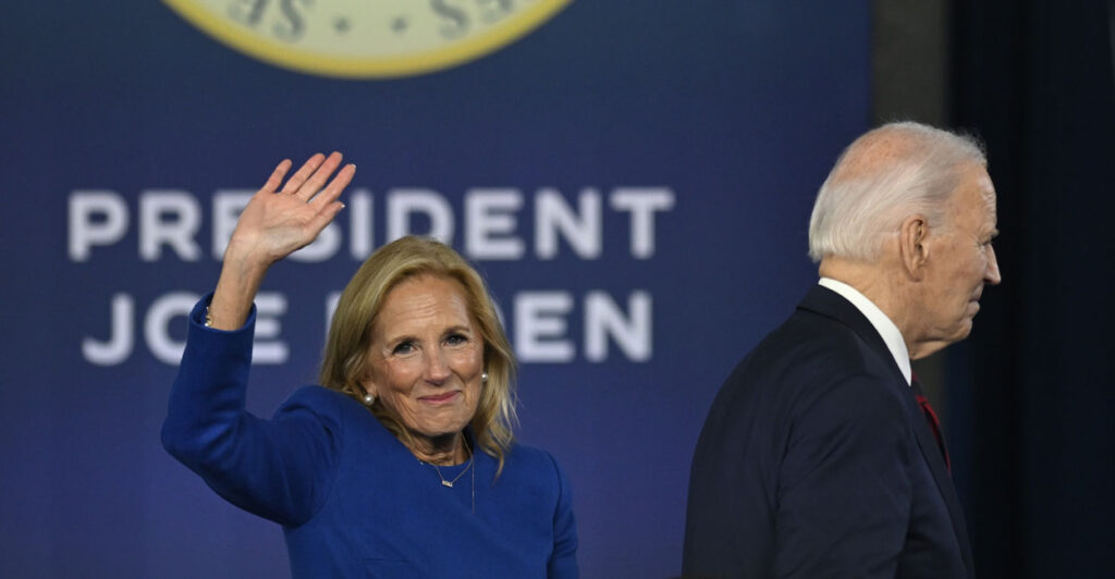 Joe Biden turns away as Jill Biden waves in front of sign reading "President Joe Biden."
