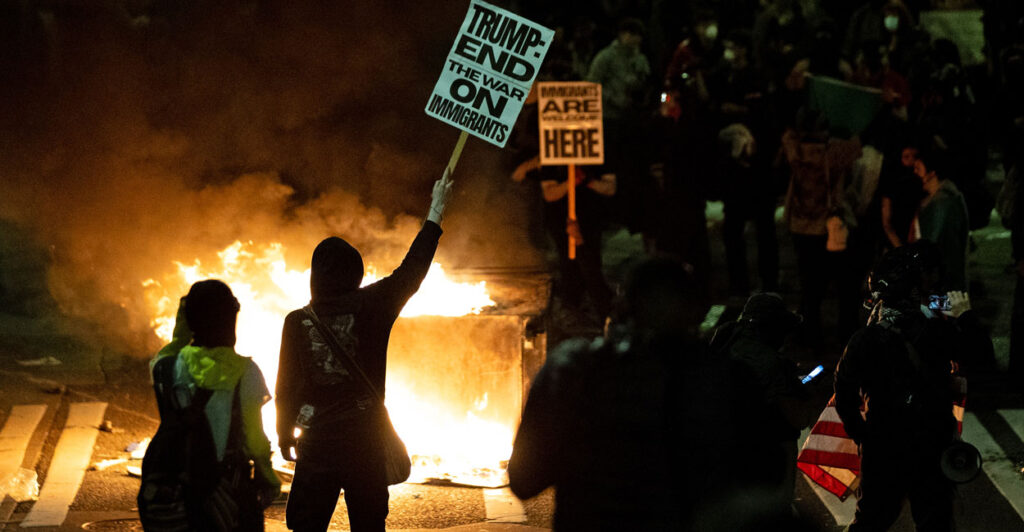 A demonstrator hoists a sign in front of a dumpster that was set on fire during a nighttime protest against federal immigration arrests on June 11 in Seattle, Washington.