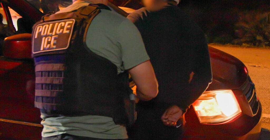 ICE agent holds a handcuffed suspect.