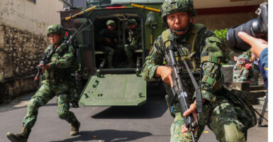 Armed Taiwanese soldiers emerge from an armored vehicle on a street.