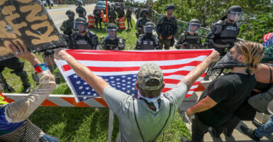 "No Kings" protesters square off against police officers. Man holds upside down American flag in their face.