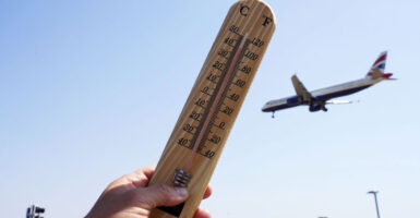Hand holds up thermometer as airplane flies in the background.