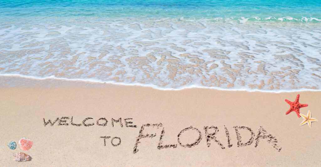 A beautiful beach with turquois water and "Welcome to Florida" written in the sand.