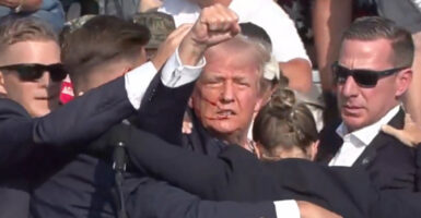 A blooded Donald Trump raises his fist while being assisted by Secret Service agents after being wounded in July 13, 2024 assassination attempt.