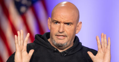 Senator John Fetterman in a dark hoodie speaks and gestures with his hands in the air