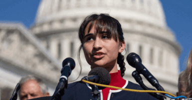 Detransitioner Chloe Cole speaks into a microphone with the Washington, DC Capitol building in the background.