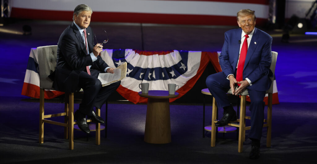 Donald Trump and Fox News host Sean Hannity sit in chairs in front of flag bunting during a 2024 town hall.