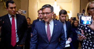 House Speaker Mike Johnson speaks while walking toward the camera, followed by members of both Congress and press.